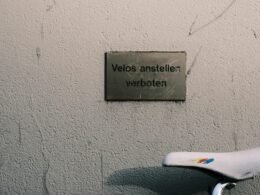 Fahrrad steht neben einer Mauer mit gut sichtbarem Schild, aufgenommen in einem städtischen Umfeld