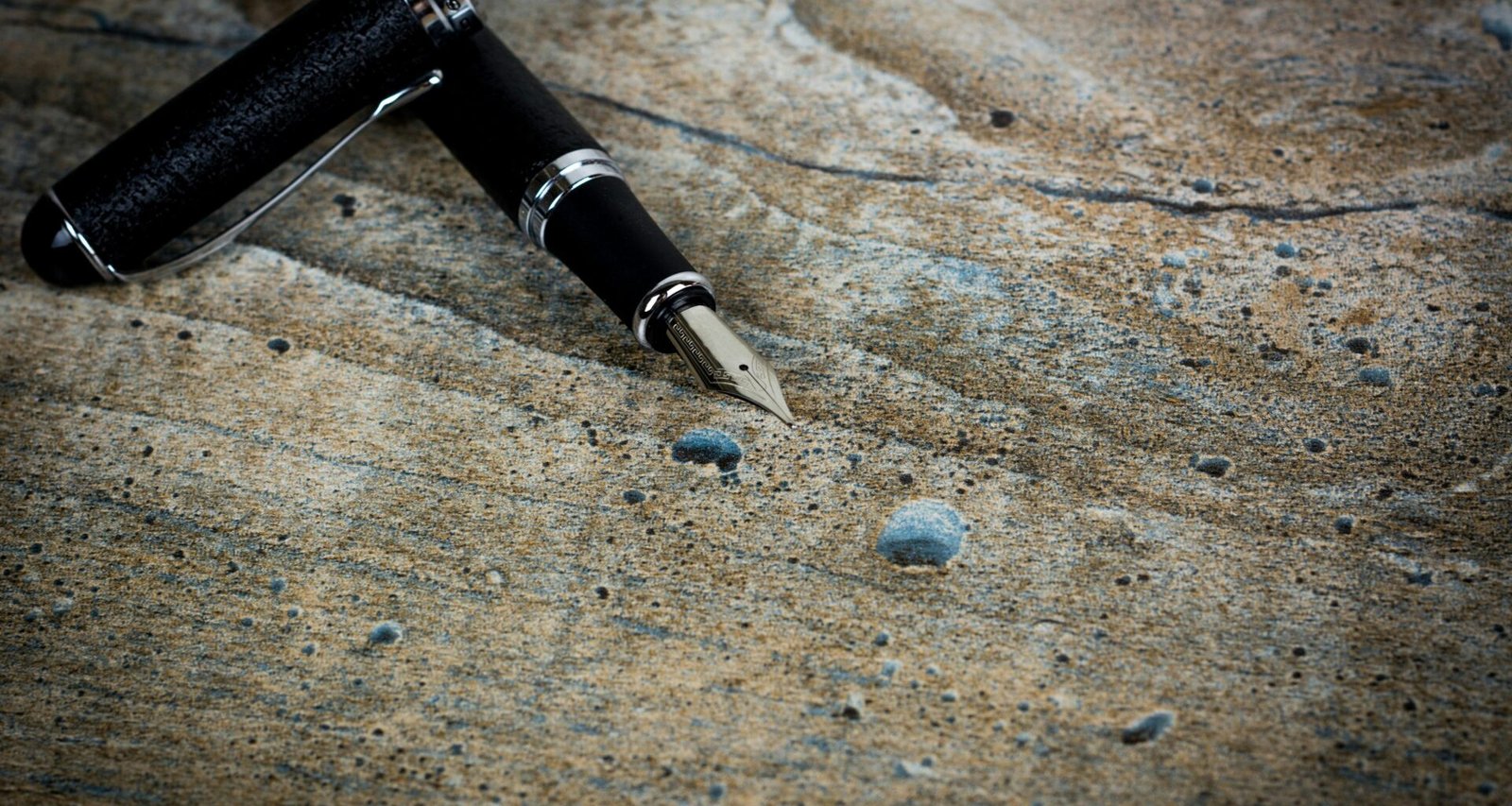 Ein schwarzer Füllfederhalter liegt waagerecht auf einem strukturierten grauen Stein im Fokus der Aufnahme.
