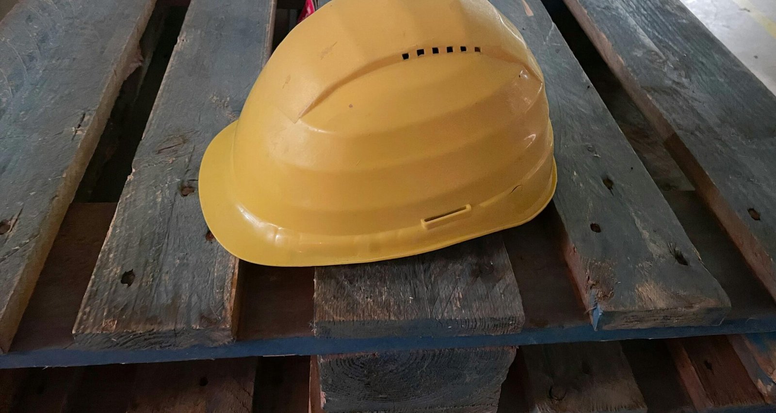 Gelber Bauhelm auf Holzpalette, authentisches Symbol für Arbeitssicherheit auf Baustellen oder industriellen Umgebungen