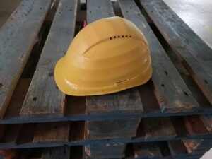 Gelber Bauhelm auf Holzpalette, authentisches Symbol für Arbeitssicherheit auf Baustellen oder industriellen Umgebungen