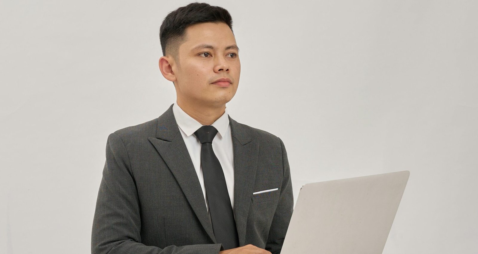 Ein Geschäftsmann im Anzug hält ein aufgeklapptes Laptop in den Händen und schaut nach oben in einem modernen Büro.