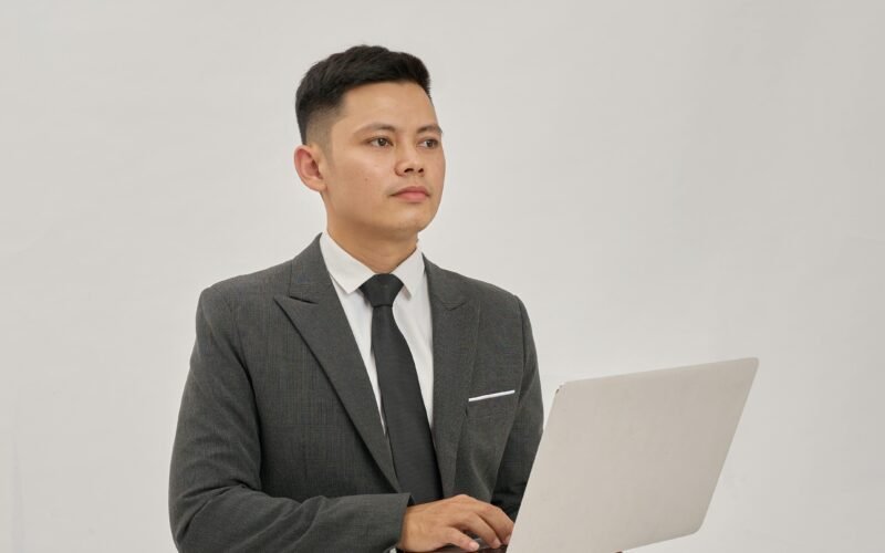 Ein Geschäftsmann im Anzug hält ein aufgeklapptes Laptop in den Händen und schaut nach oben in einem modernen Büro.