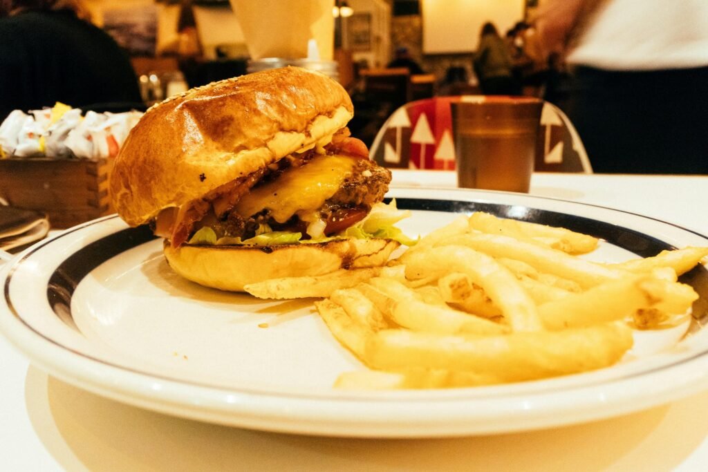 Ein Hamburger mit Salat, Tomate und Käse sowie eine Portion Pommes liegen auf einem weißen Teller