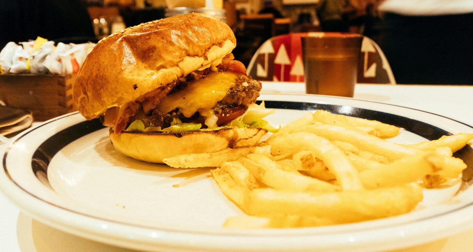 Ein Hamburger mit Salat, Tomate und Käse sowie eine Portion Pommes liegen auf einem weißen Teller