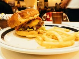 Ein Hamburger mit Salat, Tomate und Käse sowie eine Portion Pommes liegen auf einem weißen Teller