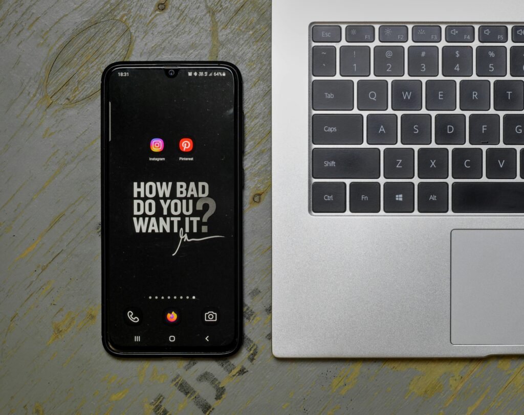 Ein Mobiltelefon liegt neben einem aufgeklappten Laptop auf einem Schreibtisch, beide Geräte sind einsatzbereit.