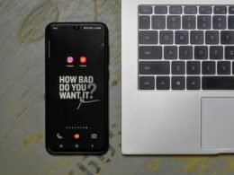 Ein Mobiltelefon liegt neben einem aufgeklappten Laptop auf einem Schreibtisch, beide Geräte sind einsatzbereit.