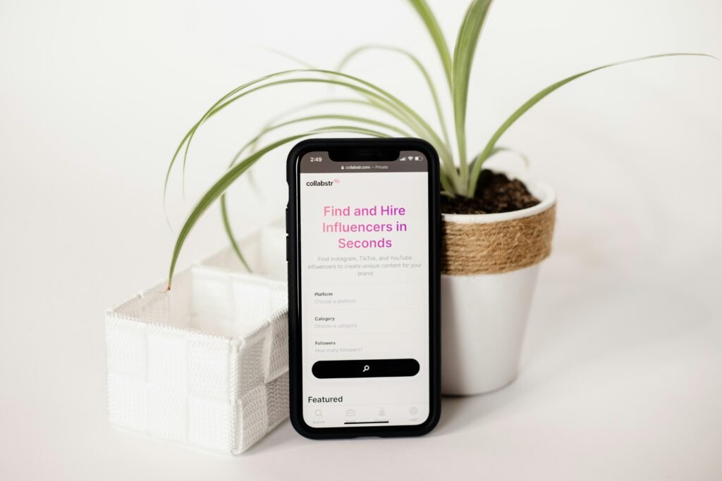 Ein Handy liegt neben einem Blumentopf mit kleiner Pflanze auf einem Tisch, ideal für Themen wie Digitalisierung und Alltagstechnik.