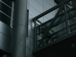 Ein hoher Metallmast steht unmittelbar neben einem mehrstöckigen Gebäude im städtischen Raum.