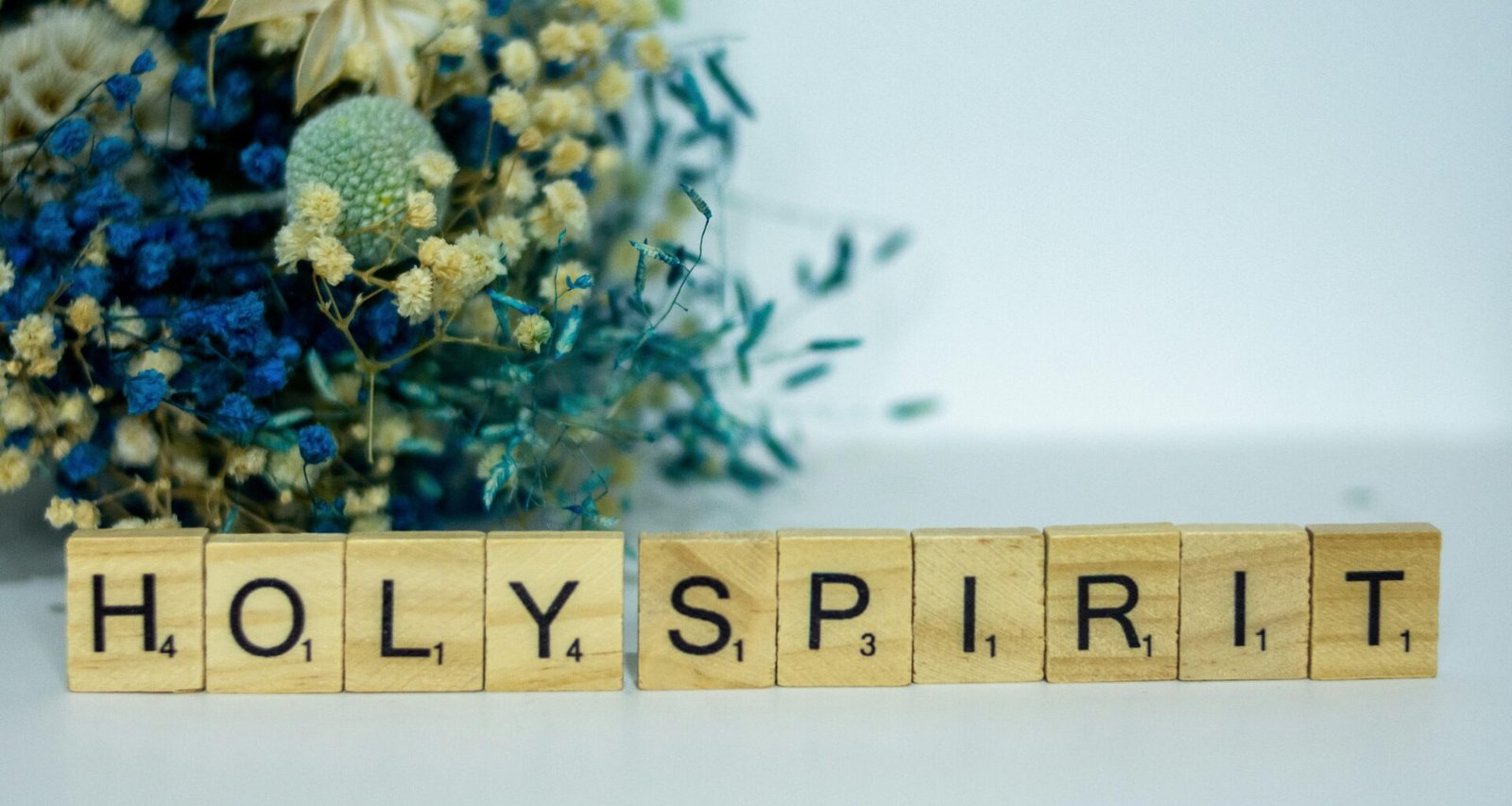 Holzblock mit dem Wort Holy Spirit und einem Blumenstrauß daneben auf hellem Hintergrund