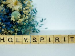 Holzblock mit dem Wort Holy Spirit und einem Blumenstrauß daneben auf hellem Hintergrund