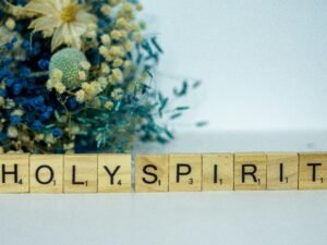 Holzblock mit dem Wort Holy Spirit und einem Blumenstrauß daneben auf hellem Hintergrund