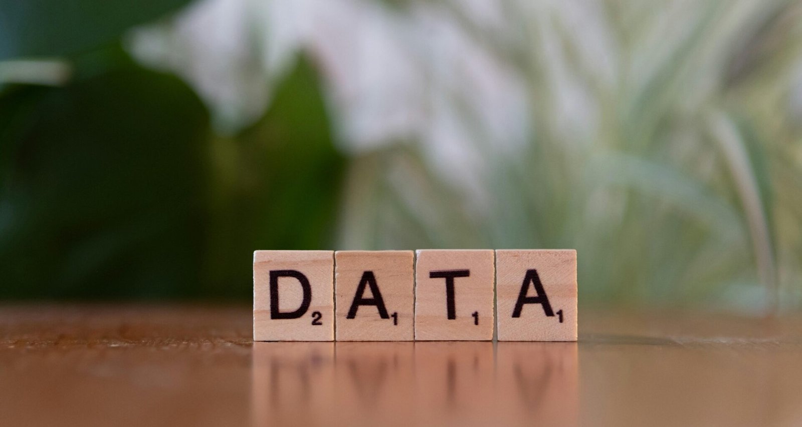 Vier hölzerne Blöcke mit den Buchstaben DATA auf einem Holztisch, sinnbildlich für Datenmanagement und Technologie.