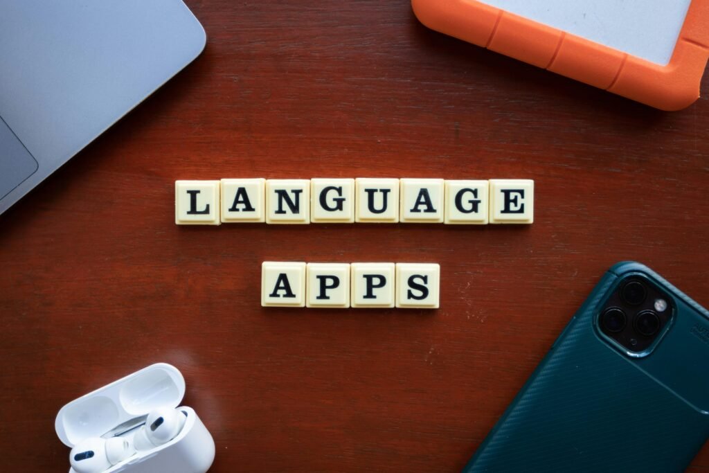 Ein Smartphone und zwei Scrabble-Spielsteine auf einem hellen Holztisch, sinnbildlich für digitale Sprache.