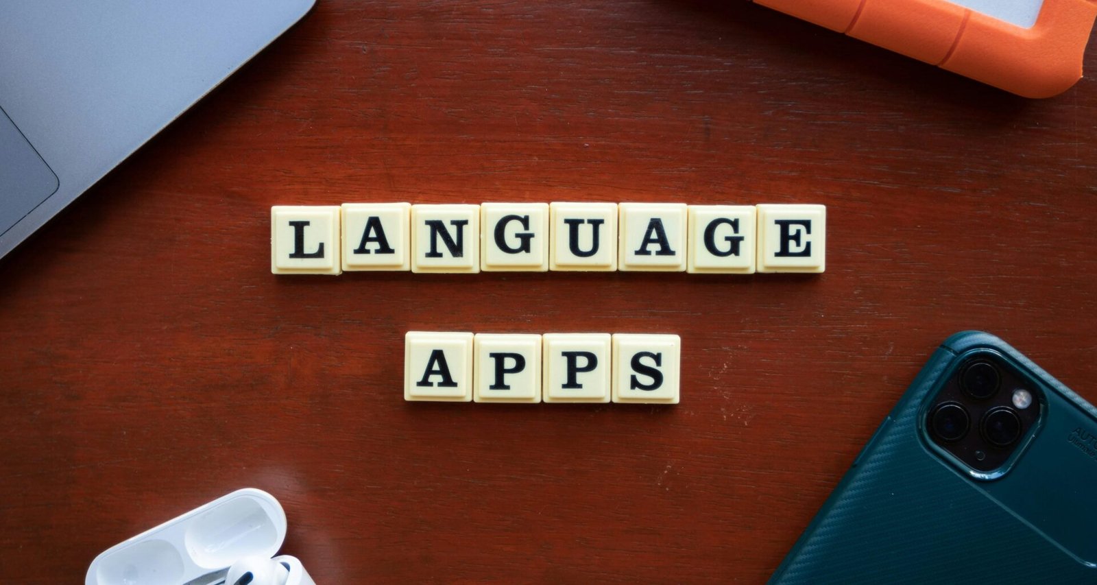 Ein Smartphone und zwei Scrabble-Spielsteine auf einem hellen Holztisch, sinnbildlich für digitale Sprache.