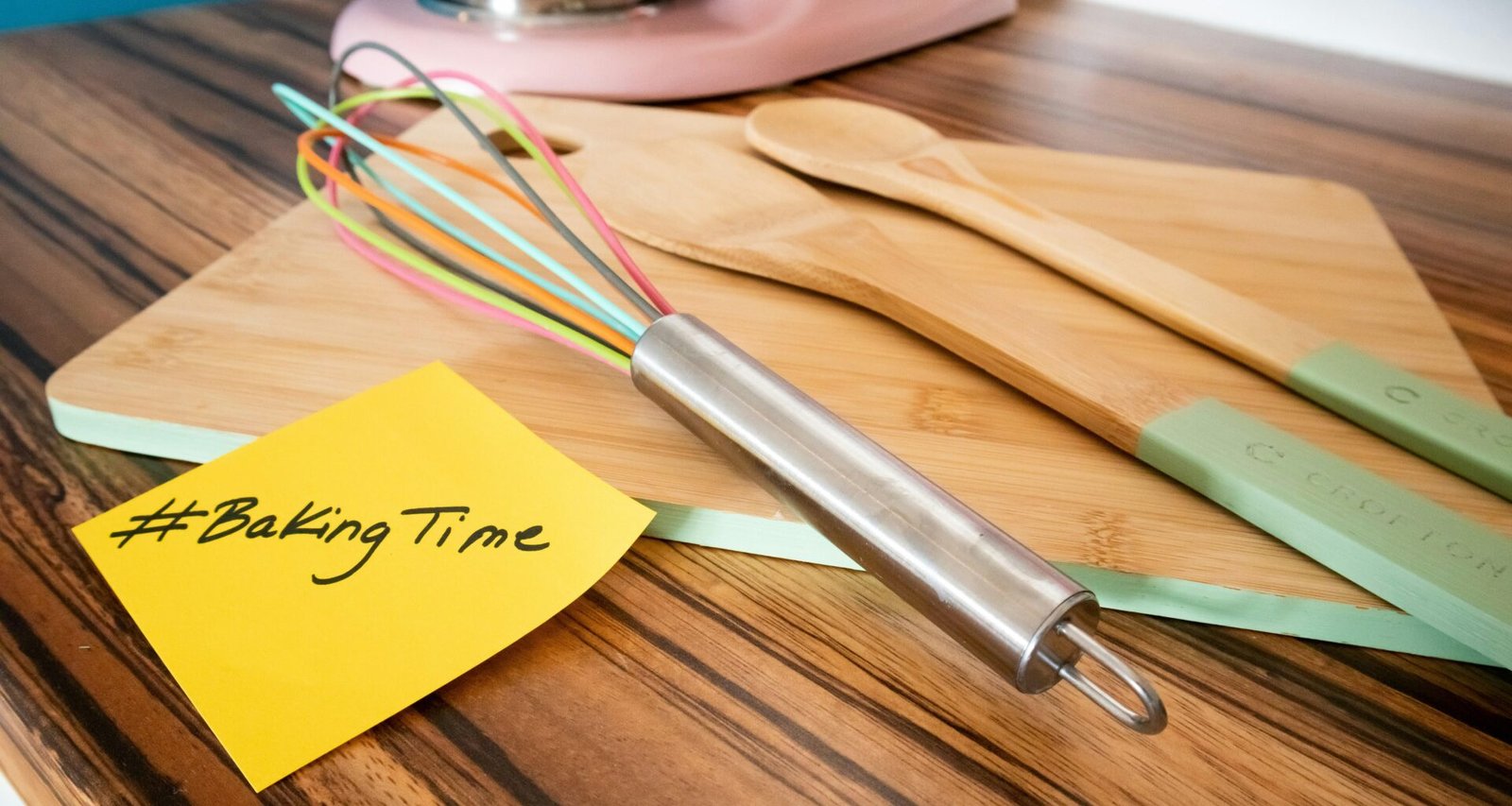 Ein Holzarbeitstisch mit einem Schneebesen und einem gelben Haftnotizzettel als Symbol für Kreativität und Planung