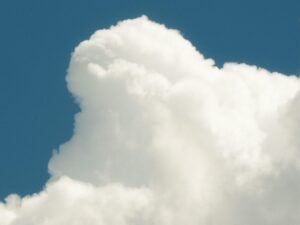 Ein Jet fliegt durch einen mit weißen Wolken bedeckten blauen Himmel, aufgenommen aus der Bodenperspektive.