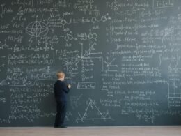 Junge steht vor einer Schultafel, die vollständig mit mathematischen Gleichungen und Formeln bedeckt ist