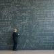 Junge steht vor einer Schultafel, die vollständig mit mathematischen Gleichungen und Formeln bedeckt ist