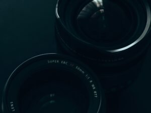 Kameraobjektiv liegt im Fokus, aufgenommen vor einem tiefschwarzen Hintergrund, technische Details sind gut erkennbar