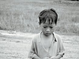 Ein Junge steht auf einem weiten Feld und hält ein Frisbee in der Hand, bereit zum Werfen an einem sonnigen Tag.