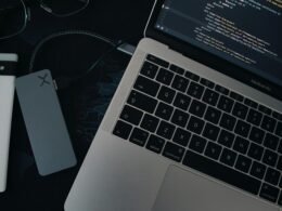 Ein moderner Laptop steht auf einem hellen Schreibtisch mit Hintergrundlicht und Zubehör, ideal für Arbeit im Homeoffice oder Büro.