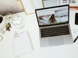 Ein moderner Laptop steht geöffnet auf einem weißen Schreibtisch in einem hellen Arbeitsumfeld mit minimalistischem Design.