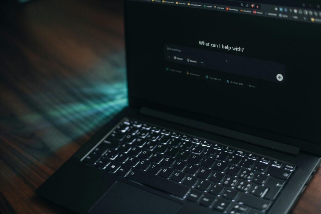 Ein geöffneter Laptop mit einer angezeigten Suchleiste und der Frage, wie geholfen werden kann, auf einem Schreibtisch