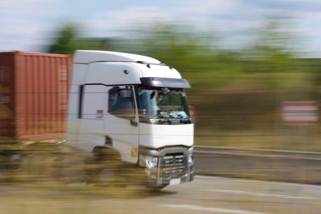 Ein Lkw fährt tagsüber auf einer asphaltierten Landstraße. Im Hintergrund ist eine weite Landschaft zu sehen.