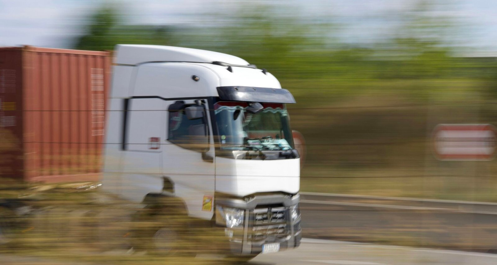 Ein Lkw fährt tagsüber auf einer asphaltierten Landstraße. Im Hintergrund ist eine weite Landschaft zu sehen.