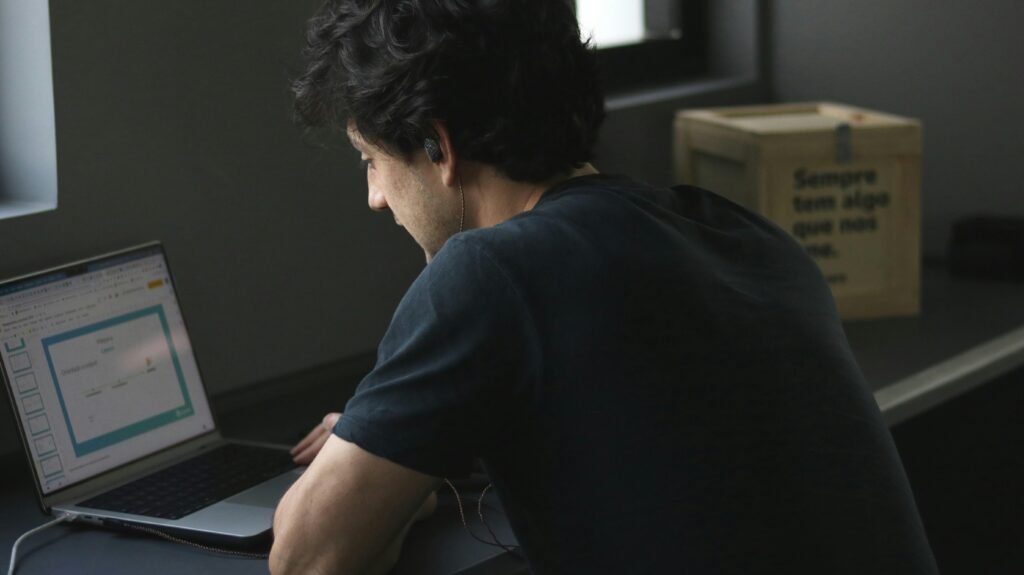 Ein Mann sitzt an einem Tisch und arbeitet konzentriert an seinem Laptop, umgeben von moderner Technik.