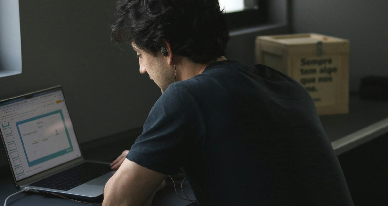 Ein Mann sitzt an einem Tisch und arbeitet konzentriert an seinem Laptop, umgeben von moderner Technik.