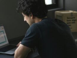 Ein Mann sitzt an einem Tisch und arbeitet konzentriert an seinem Laptop, umgeben von moderner Technik.