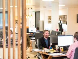 Ein Mann sitzt an einem Schreibtisch in einem modernen Büro und arbeitet konzentriert an seinem Computer.