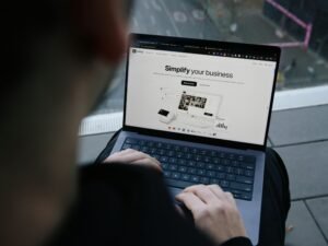 Ein Mann sitzt im Freien auf einer Bank und nutzt einen Laptop für mobiles Arbeiten oder Online-Kommunikation.