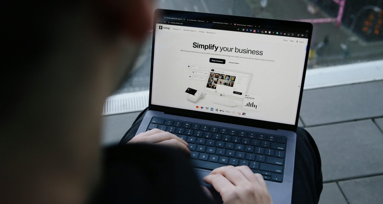 Ein Mann sitzt auf einer Bank im Freien und arbeitet mit seinem Laptop Computer