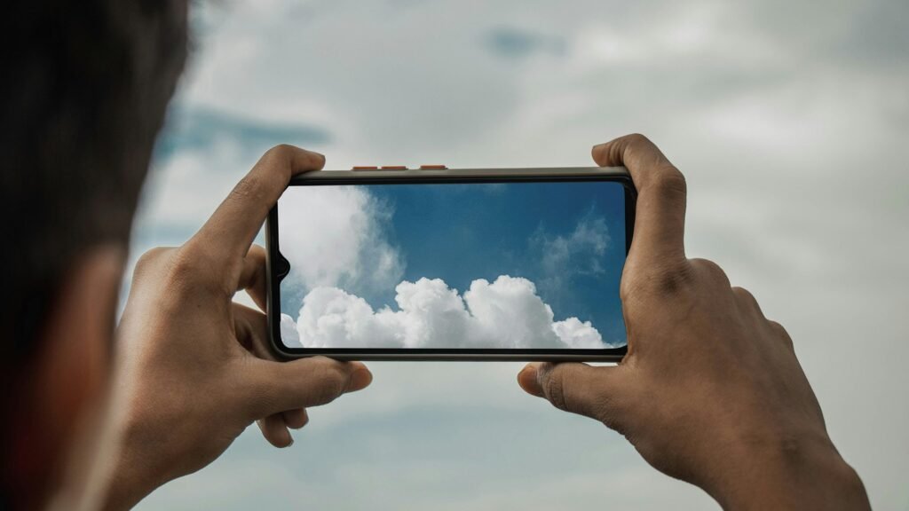 Ein Mann richtet seine Kamera auf eine isolierte Wolke am blauen Himmel, um das Wolkenmotiv fotografisch festzuhalten.