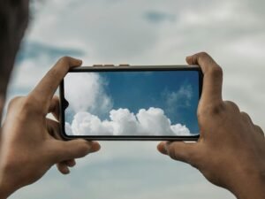 Ein Mann richtet seine Kamera auf eine isolierte Wolke am blauen Himmel, um das Wolkenmotiv fotografisch festzuhalten.