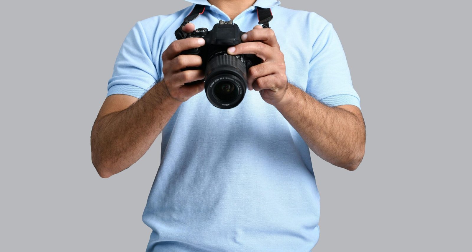 Ein Mann steht mit einer Kamera in der Hand vor neutralem Hintergrund – Symbolbild für Fotografie und Technik.