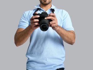 Ein Mann steht mit einer Kamera in der Hand vor neutralem Hintergrund – Symbolbild für Fotografie und Technik.