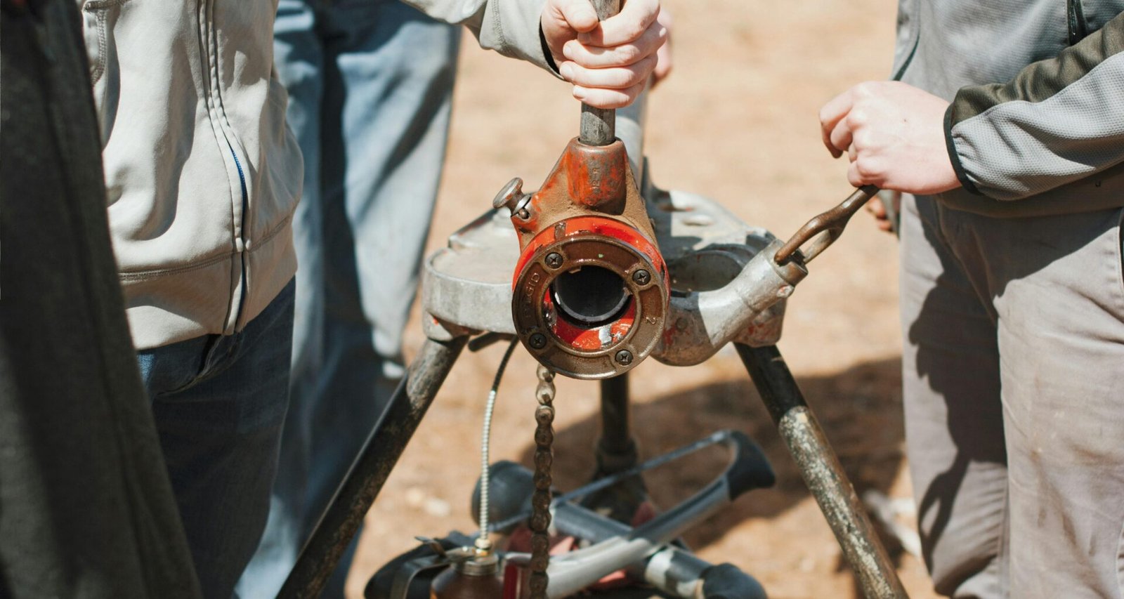 Zwei Männer in Arbeitskleidung, einer hält einen Schraubenschlüssel, gemeinsam vor neutralem Hintergrund im Technikbereich
