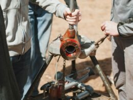 Zwei Männer in Arbeitskleidung, einer hält einen Schraubenschlüssel, gemeinsam vor neutralem Hintergrund im Technikbereich