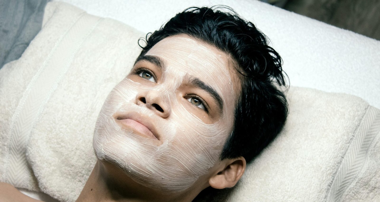 Mann liegt auf einem Bett mit einem weißen Handtuch auf dem Kopf, entspannt im Schlafzimmer