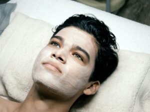 Mann liegt auf einem Bett mit einem weißen Handtuch auf dem Kopf, entspannt im Schlafzimmer