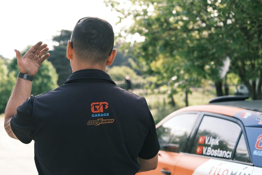 Ein Mann steht neben einem geparkten Auto auf einer Straße in städtischer Umgebung, fotografiert bei Tageslicht.