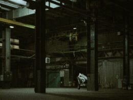 Ein Mann fährt auf einem Motorrad eine Straße entlang, flankiert von hohen Gebäuden und moderner Architektur.