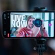 Ein Mann nimmt sich mit einem Smartphone auf, das auf einem Stativ befestigt ist, ideal für Videoproduktion oder Vlogging.