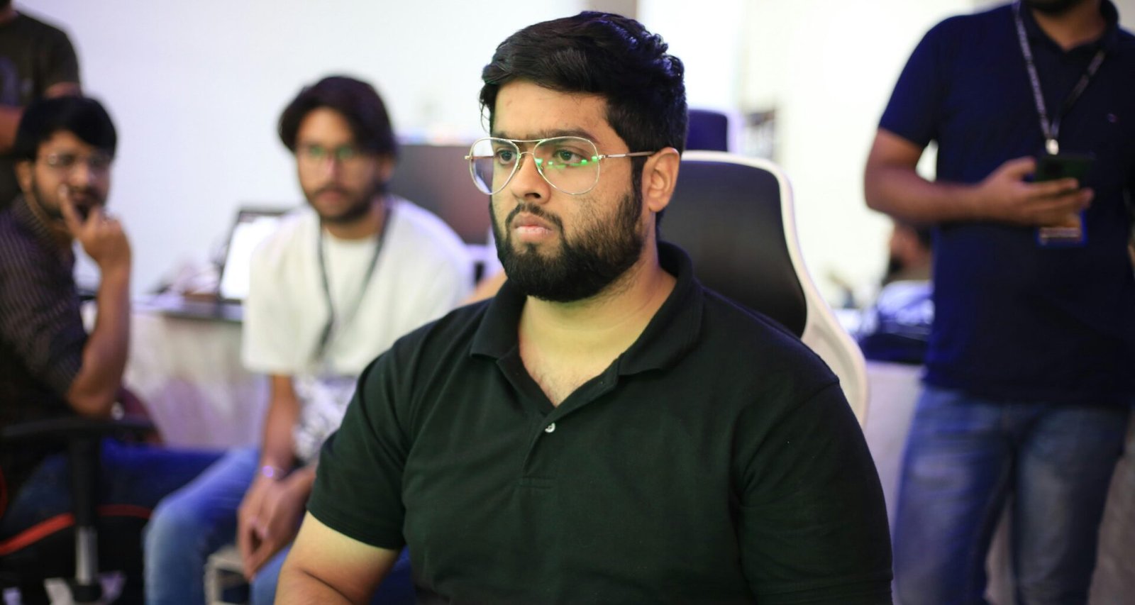 Ein Mann mit Brille sitzt an einem Tisch und spricht vor einer Gruppe von Personen, die aufmerksam zuhören.