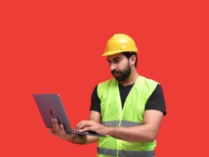 Ein Mann mit gelbem Schutzhelm hält ein Tablet und überprüft Baupläne vor Ort auf einer Baustelle.