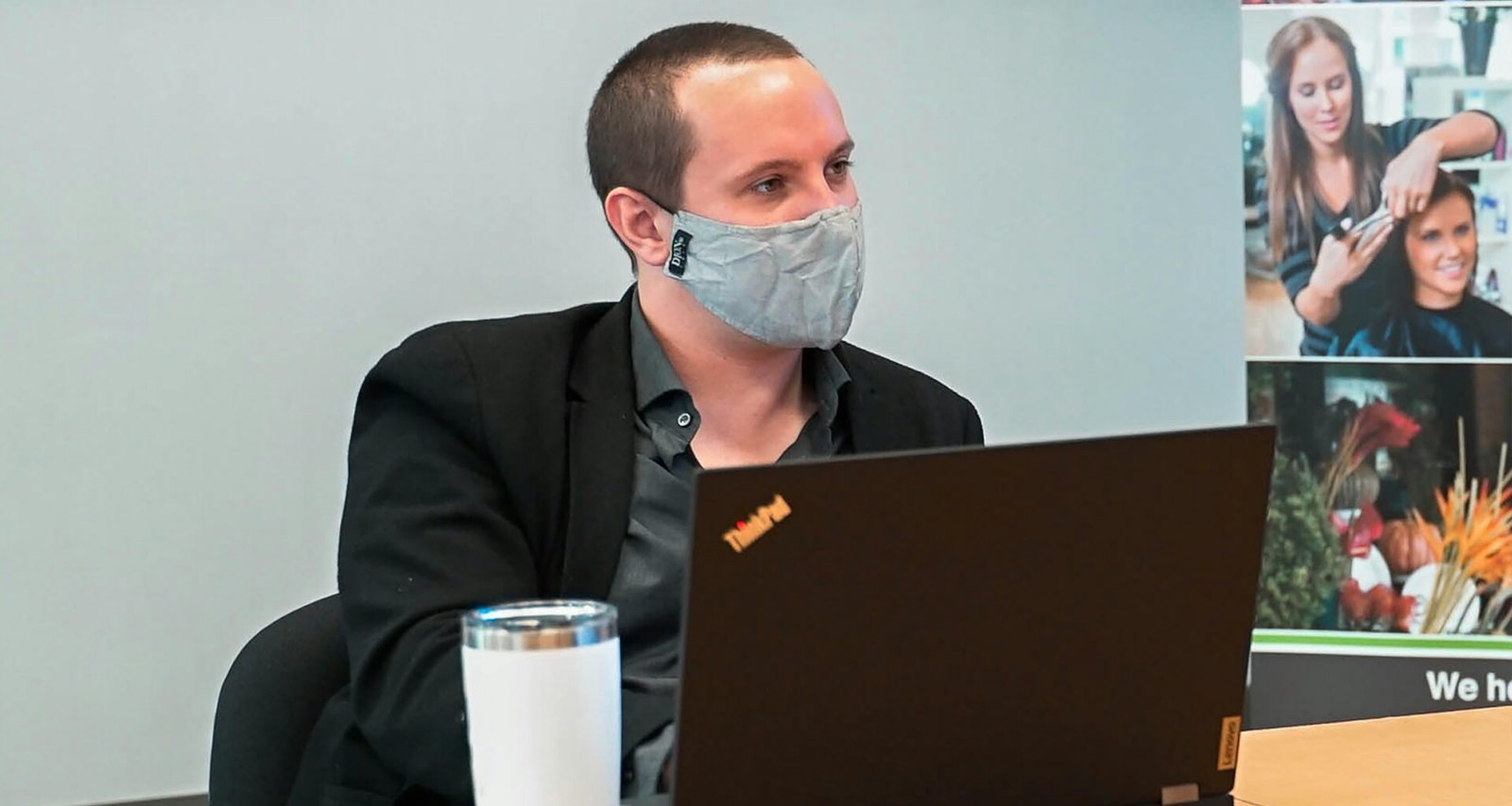 Ein Mann mit Gesichtsmaske sitzt vor einem Laptop an einem Schreibtisch in einem modernen Arbeitsumfeld.